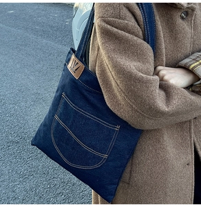 Detail of blue denim tote bag with yellow contrast stitching and leather logo on brown coat