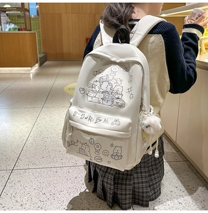Detail of cream cartoon backpack featuring black line art illustrations and plush charm