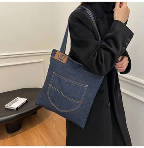 Detail of dark blue denim tote bag with brown leather logo patch and visible stitching