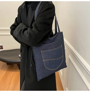 Detail of blue denim tote bag with orange contrast stitching worn with a black coat