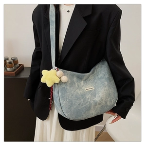 Close-up of light blue denim crescent bag featuring star plush charm and pompom detail