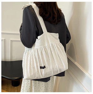 Close-up of a white polka dot tote bag featuring ruffled details and a Romance label