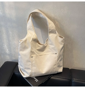 Detail of creamy corduroy tote bag featuring external pocket and metal rivet accents