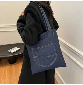 Detail of blue denim tote bag showing yellow contrast stitching and shoulder strap