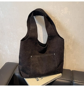 Detail of black corduroy tote bag showing white stitching and silver rivets on the pocket