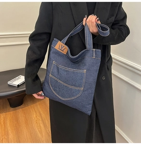 Detailed close-up of dark blue denim tote bag with brown leather logo patch and pocket