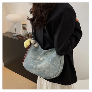 Detailed shot of large denim blue hobo bag with charms on model in casual suit