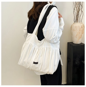 Close-up of white pleated tote bag with Romance logo label and textured fabric detail