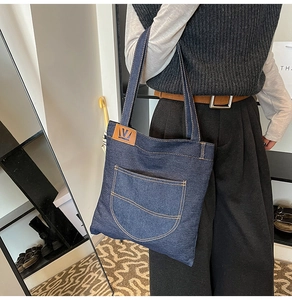 Detailed view of the dark blue denim tote bag featuring a stitched front pocket and leather patch