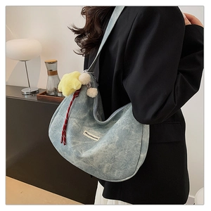 Close-up of blue denim hobo bag with yellow star plush and white puff pendant detail