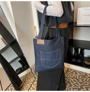 Detail of dark blue denim tote bag featuring a leather logo patch and practical front pocket