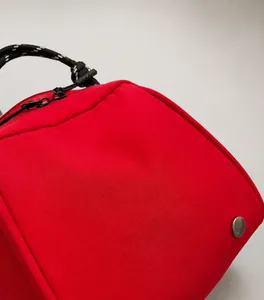 Detailopname van rode tas van getextureerd nylon met geweven handvat en metalen knop