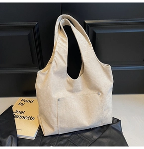 Detail of beige corduroy tote bag showing ribbed texture and metal rivet on front pocket