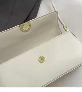 Close-up of the elegant gold magnetic snap closure on a cream leather underarm bag