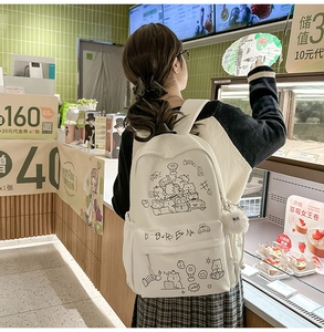 Back view of a white canvas backpack with cute black line-art cartoon doodles and pom pom