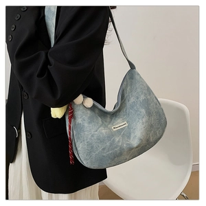 Detail of light blue denim texture shoulder bag with brand patch and decorative tassel