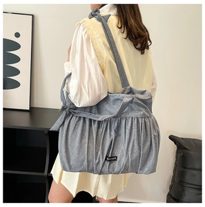 Detail of blue denim tote bag featuring stylish pleats and a decorative bow strap accent