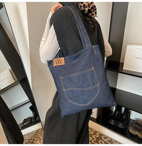 Detail of deep blue denim tote bag featuring large front pocket and brown leather logo tag