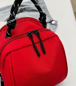Detail van een rode nylon rugzak met gladde zwarte dubbele ritsen en geweven handvat