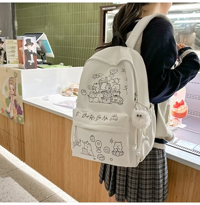 Close-up of white cartoon backpack with black animal doodles and plush pompom charm