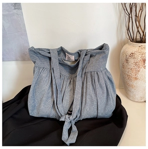 Detail of grey pleated tote bag with knot strap on minimalist background with vase