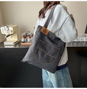 Detail of gray denim tote bag featuring orange contrast stitching and leather brand tag