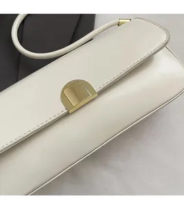 Detail of cream shoulder bag featuring gold semi-circular magnetic buckle and sleek texture