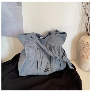 Detail of grey pleated tote bag featuring knotted shoulder strap and Romance label