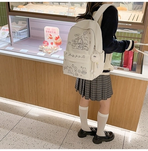 Cute cream white canvas backpack with cartoon animals and plush ball charm in a cafe