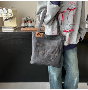 Detail of dark grey denim tote bag with brown leather logo patch and front pocket