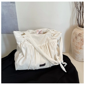 Detailed close-up of white pleated tote bag featuring Romance black woven label