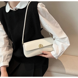 Close-up of minimalist cream underarm bag with gold metal clasp on model's shoulder