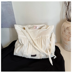 Close-up of white pleated canvas tote bag with romance label and casual knotted strap