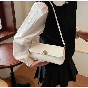 White minimalist leather shoulder bag with gold metal buckle shown on a model in a cafe