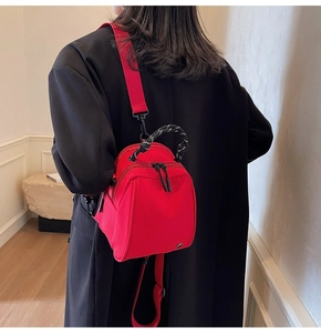 Close-up of bright red nylon shell bag worn by model with woven handle and shoulder strap