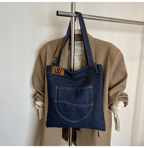 Close-up of deep blue denim tote bag with large double-stitched pockets and leather logo
