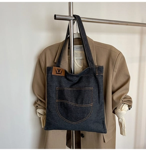 Detail of blue denim tote bag featuring a front pocket and brown leather logo patch