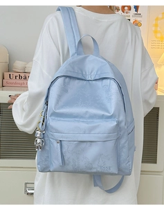 Detail of light blue nylon backpack with floral texture and silver bear charm