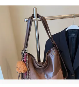 Detail of dark brown tote bag with contrast textures and a cute bear keychain accessory