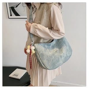 Detail of light blue corduroy crescent bag with wide strap and pompom charm decoration