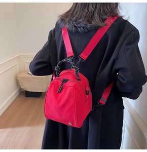 Close-up of a red mini shell-shaped backpack with contrast woven handle and double zippers