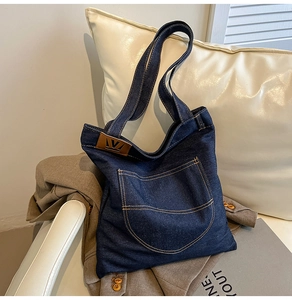 Detail of dark blue denim tote bag with leather trim and v-metal decoration on a sofa