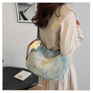 Detail of light blue denim crescent bag with star plush charm on a model's shoulder