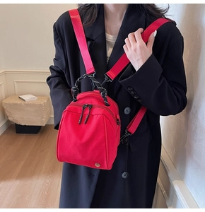 Close-up of red mini shell backpack with dual zippers and woven handle on black coat