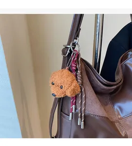 Detail of a brown plush poodle charm hanging on a leather tote bag with silver ring