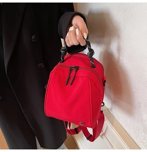 Detail of red nylon backpack with woven handle and dual zippers held by a model