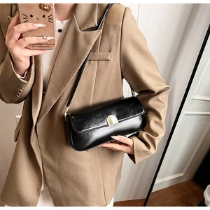 Detail of black glossy leather underarm bag featuring a elegant gold semi-circle metal clasp