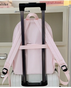Light pink backpack with a practical luggage strap for travel, shown on a suitcase