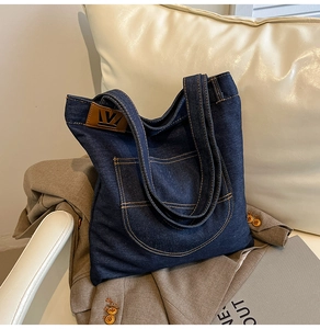 Detailed view of dark blue denim tote bag with contrast stitching and leather brand tag