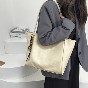 Detalle de un bolso tote de cuero blanco crema con un colgante de borla tejida marrón